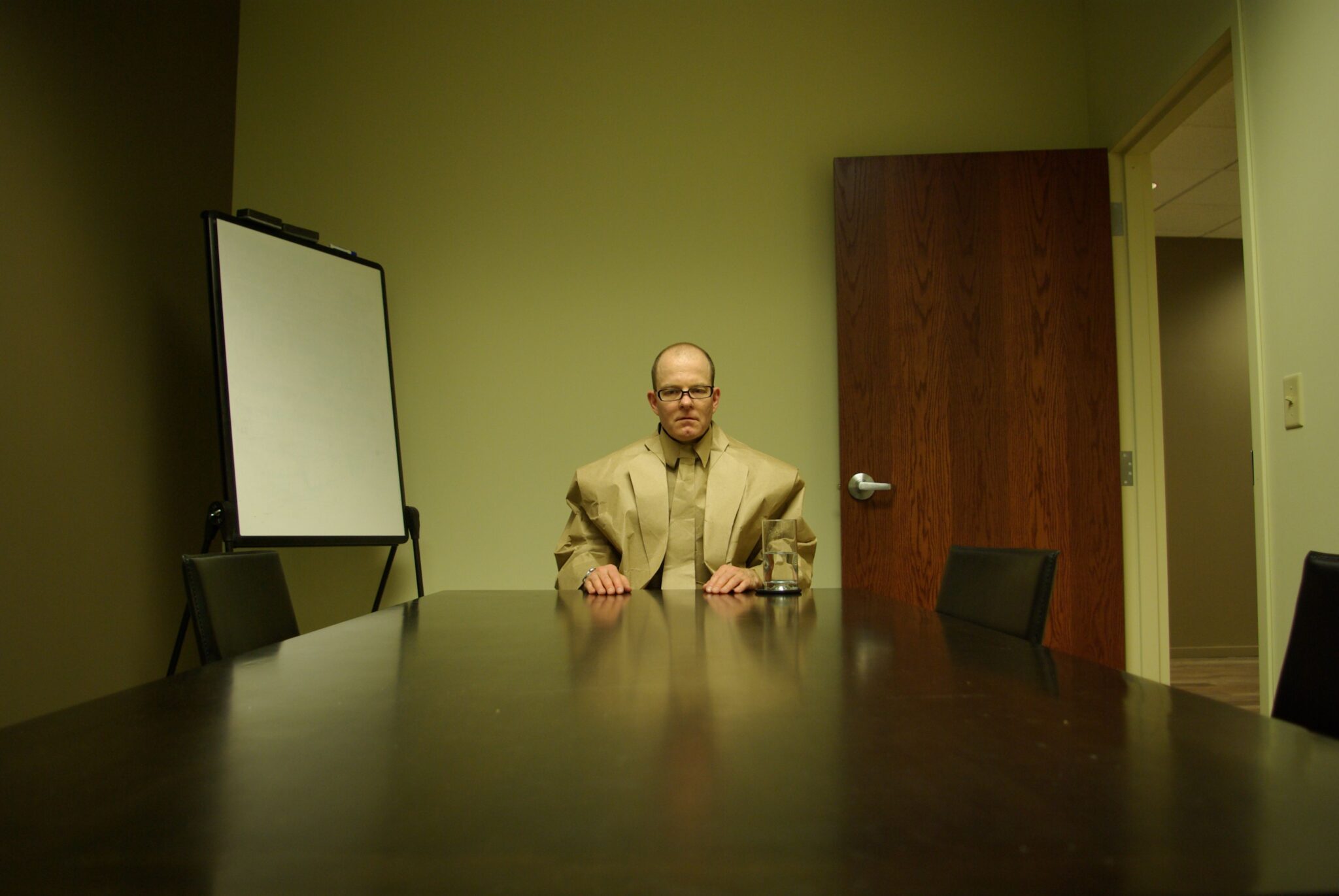 A man in a brown paper suit sitting at a conference table in an office